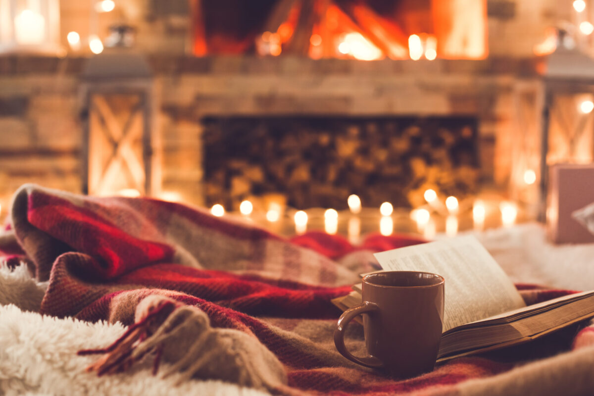 Book, blanket and ceramic mug by a fireplace.